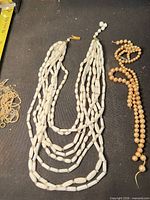 Overview of multi-strand white bead necklace, peach pearl necklace, loose findings