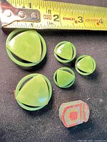 overview of five green Bakelite dress clips next to ruler and painted metal box