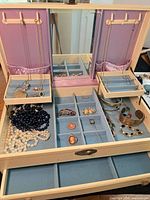Overview of open jewelry box showing necklaces, bracelets, brooch, bead strands, faux pearls
