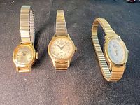 Front view of three gold-tone Timex women’s wrist watches on black background