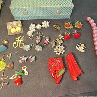 Overview of assorted earrings, brooches, charms and findings on black surface