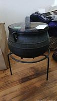 Side view of antique cast iron pot on metal stand showing pot shape, stand legs and side handle.
