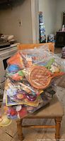 Photo of a large clear bag filled with assorted toys in plastic packaging, placed on a wooden chair.