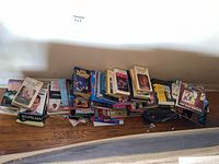 Photo of multiple stacks of paperback books on a wooden floor including GOR series, Roger Zelazny titles, and various others.