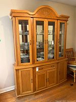 Front view of solid wood china cabinet with glass door hutch showing interior shelving with dishes inside. The lower buffet storage cabinet with drawer is visible.