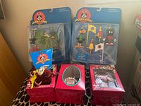 Photo showing complete lot including two packaged action figure sets (Duck Dodgers with Marvin the Martian, Road Runner with Wile E Coyote), Tasmanian Devil keyring, and two red boxed Tasmanian Devil Christmas ornaments, all new in packaging.