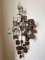 Front view of metal 3D wall art sculpture hanging on a wall, showing many rectangular metal plates with textured surfaces attached to a metal frame.