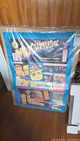 Full view of vintage MuchMusic poster shrink-wrapped and leaning against wood panel surface, showing colorful retro graphics and text.