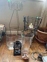 Two metal plant stands seen with one holding a ceramic floral arrangement. Three clear glass vases and a black tea light holder are placed around them on a wooden floor.