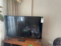 Samsung 40-inch TV on wooden stand showing front view with remote on stand.