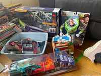 Lot overview showing sealed Zurg Mothership spaceship, Buzz Lightyear figure box, Fisher-Price playset, and multiple vehicles in packaging.