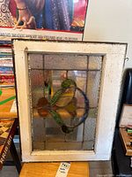 Full view of the vintage stained glass window showing central colorful floral-like design surrounded by textured clear glass and weathered white wooden frame.