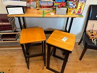 Front view of two stools with light wood tops and dark wood bases next to table with similar wood tones