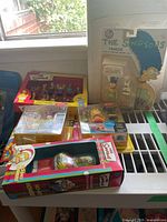 View of the entire assortment showing the boxed 12-piece miniature figure set, multiple other boxed figures including Marge and Lisa, and the poster rolled flat beneath the boxes.