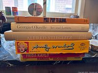 Stack of art books including Pre-Pop Warhol, Georgia O’Keeffe Art and Letters, Alfred Stieglitz, Andy Warhol puzzle box, Frida Kahlo and Warhol on Basquiat.