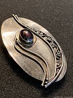 Oblique view of sterling silver brooch showing cabochon and scroll design
