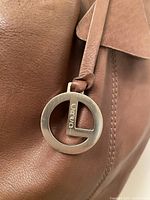 Close-up of silver-tone L.Credi logo charm on brown leather