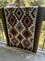 Full view of woven rug hanging over railing showing entire geometric pattern and fringe