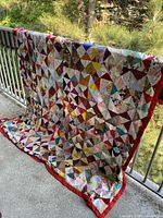 Full view of quilt draped over railing showing multicolour patchwork and red border