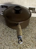 Saucepan with lid angled view showing wood handle and brown enamel
