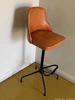 Full view of orange vinyl bar stool showing seat, backrest, and black metal base