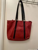 Front view of red leather tote bag hanging, showing black straps and overall shape