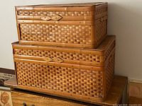 Two stacked woven wooden trunks closed showing exterior weave and clasps