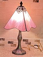 Full view of lamp illuminated, showing pink glass shade and bronze base