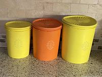 Three graduated plastic canisters, two yellow one orange, with lids on