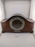 Front view of wooden mantle clock showing curved silhouette and brass bezel around clock face.