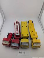 Front view of the four pressed steel trucks showing their colors and configurations including fire truck with ladder, truck cab, flatbed and car loader trucks.