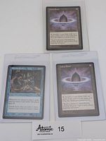 Three Magic the Gathering cards: one Rhystic Study and two Lotus Petal cards, all sleeved, displayed on a white surface with a small Atomic Collectibles label below.