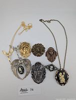 Overview photo of the collection showing the variety of necklaces and brooches including cameos, ornate faces, and bird motif.