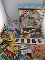 Overview of the lot showing boxed Mickey in the Kitchen plate set, Walt Disney comics, Expo 74 materials, gift certificates, and books.