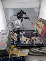 Photo of NHL hockey memorabilia including sealed Molson NHL jersey plaque, Roberto Luongo puck and card, Canucks clock, mini hockey sticks, and part of signed photo with scarf.
