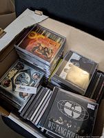 Box with multiple CD jewel cases arranged in stacks. Visible albums include Wu-Tang Forever and other mixed artists.