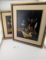 Two framed oil paintings leaning against a wall, showing their front and some frame wear.