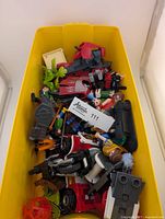 Top view of yellow storage box filled with assorted Playmobil figures and accessories including a red police motorcycle.