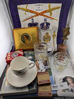 Full lot showing tea cup & saucer, glass mugs, Staffordshire ceramic box, books, magazines, souvenir items, and vintage tea towel in the background.