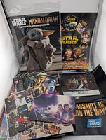 Photo showing the sealed pack of 12 The Mandalorian posters with Grogu on the cover and various Star Wars trading cards and pamphlets spread out below.