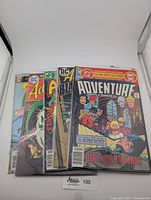 Four vintage 1970s DC comic books arranged side by side, encased in protective sleeves, titles visible Adventure Comics (Death of Batman), Aquaman, Black Orchid.