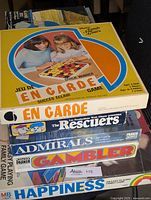 Top view of stacked vintage board games featuring En Garde, The Rescuers, Admirals, Gambler, Happiness game boxes.
