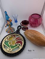 Full view of all items in the lot showing their relative size and arrangement including the musician cup, cranberry vase, ceramic cocoa pod, rooster trivet, and Flamenca figurine