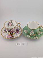Full view of two vintage teacup and saucer sets side by side, showcasing their floral and leaf patterning.