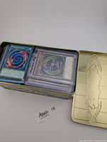 Photo of Yu-Gi-Oh! cards inside a vintage gold metal tin with embossed lid design.