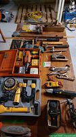Full layout of assorted hand and power tools displayed on a wooden table including saws, clamps, power tools, cases, and manuals.