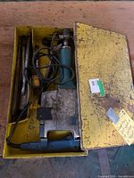 Photo showing the full jackhammer inside the open yellow metal carrying case along with chisels and power cord tangled.