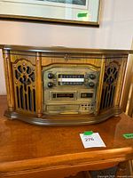 Front view of vintage-style stereo system in wood veneer, shows radio dial, cassette player, and control knobs.