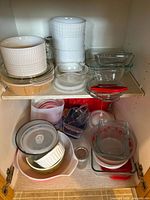 Shelf with stacked white ceramic bowls, clear glass baking dishes, plastic lids, and various mixing bowls and containers below.