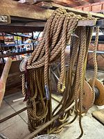 Heavy duty natural fiber twisted rope hanging on wooden rack, showing thickness and texture, used condition with minor fraying